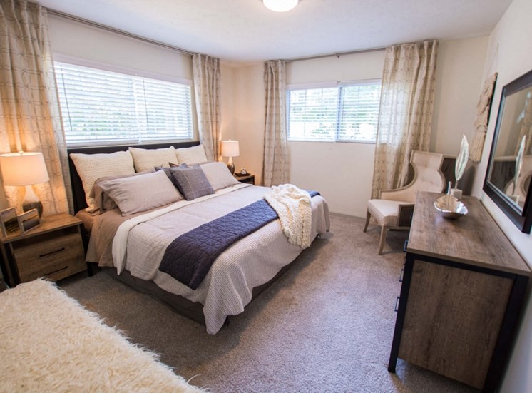 Relax in your spacious master bedroom at Icon Avondale. Big bed, dresser, carpet, big long windows, night stand, chair in corner.